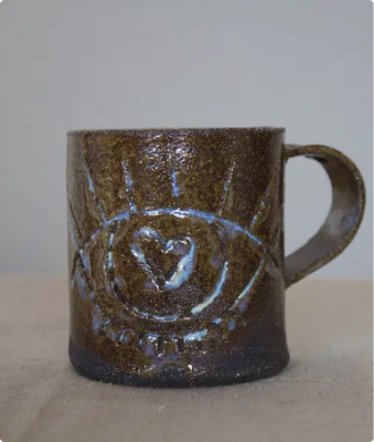 Taza de cerámica artesanal en tono marrón con motivo de ojo y corazón