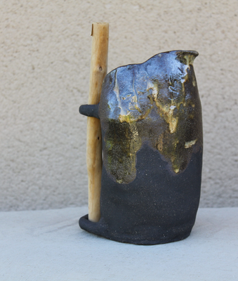Jarrón de cerámica artesanal en negro y dorado con una vara de madera