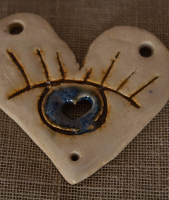 Colgante de cerámica artesanal en forma de corazón con un ojo azul, visto de cerca