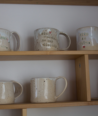 Tazas de cerámica artesanal colocadas en una estantería de madera del taller